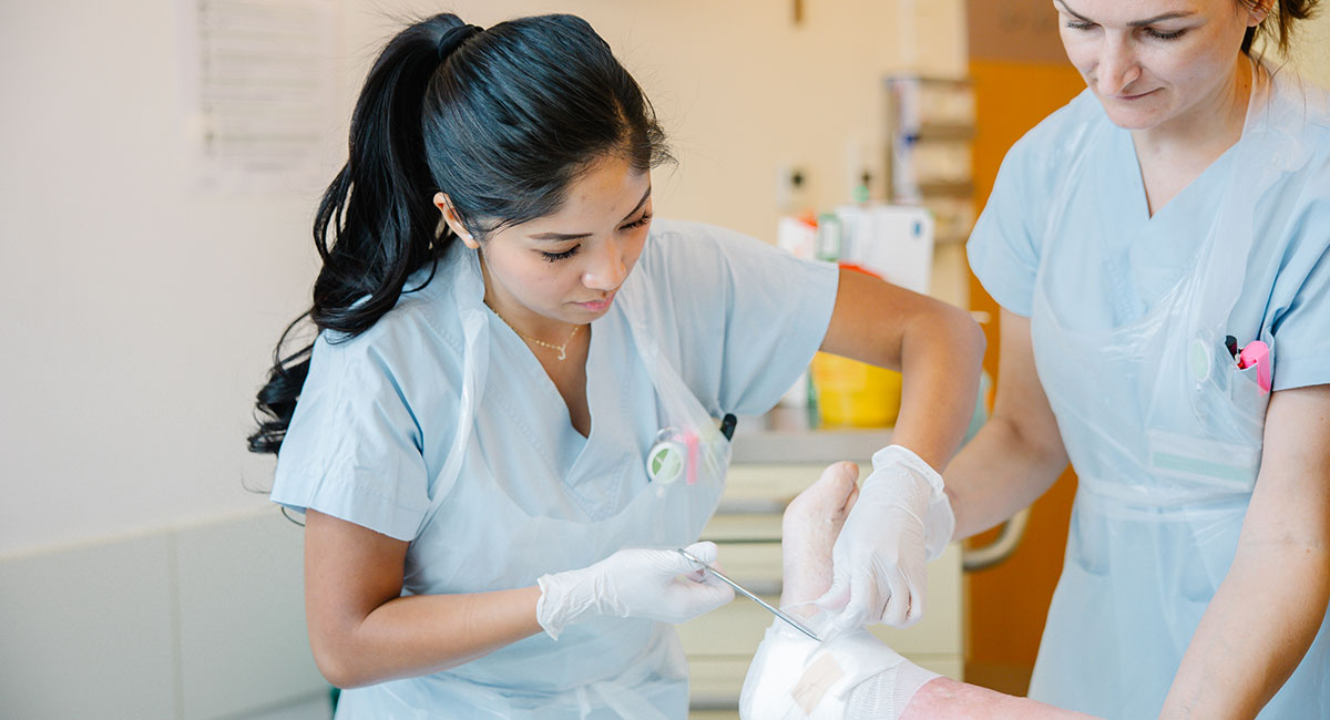 Zwei weibliche Krankenpflegepersonen versorgen eine Wunde am Fuß eines Patienten