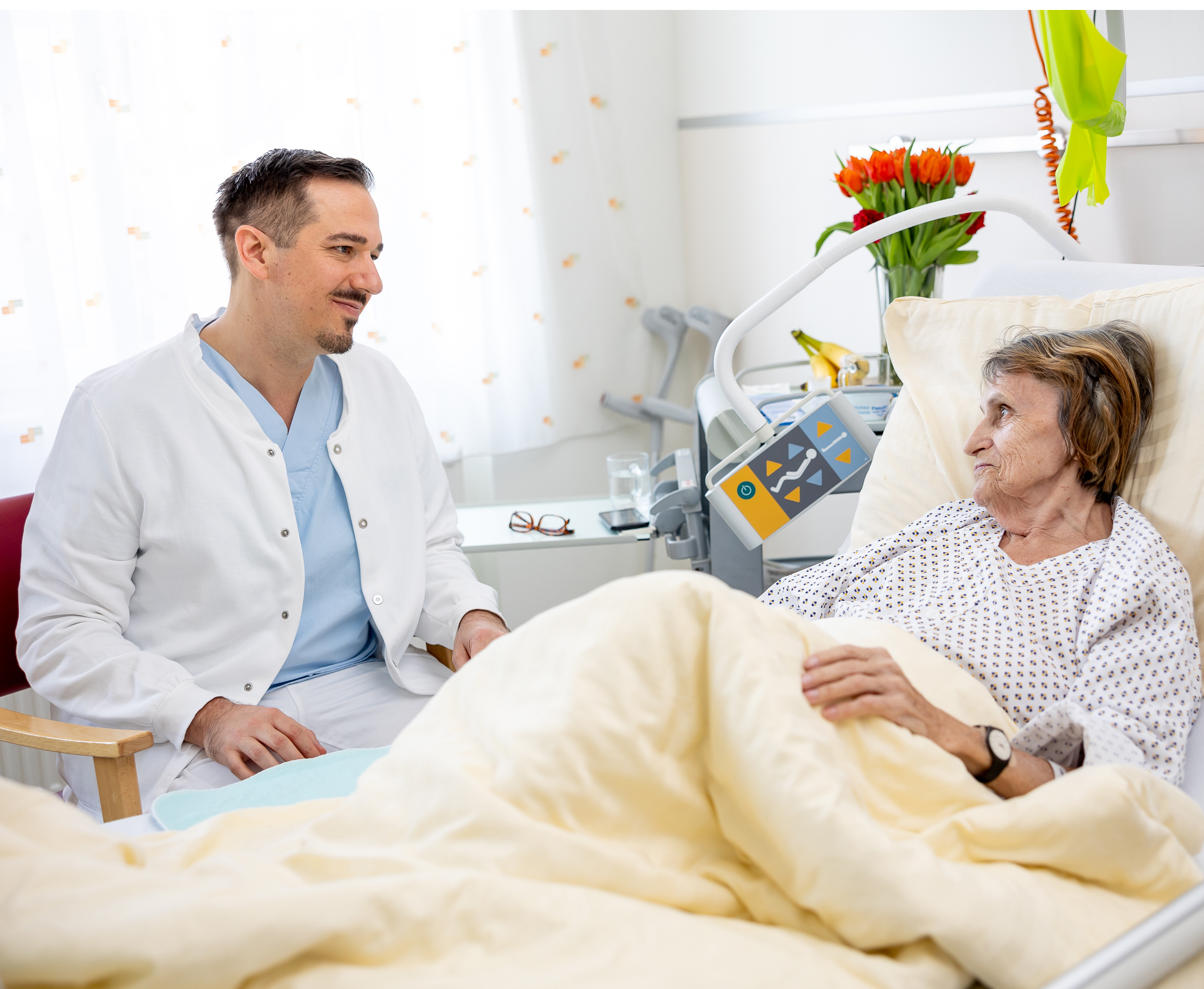 Eine männliche Pflegeperson sitzt bei einer Patientin und unterhält sich