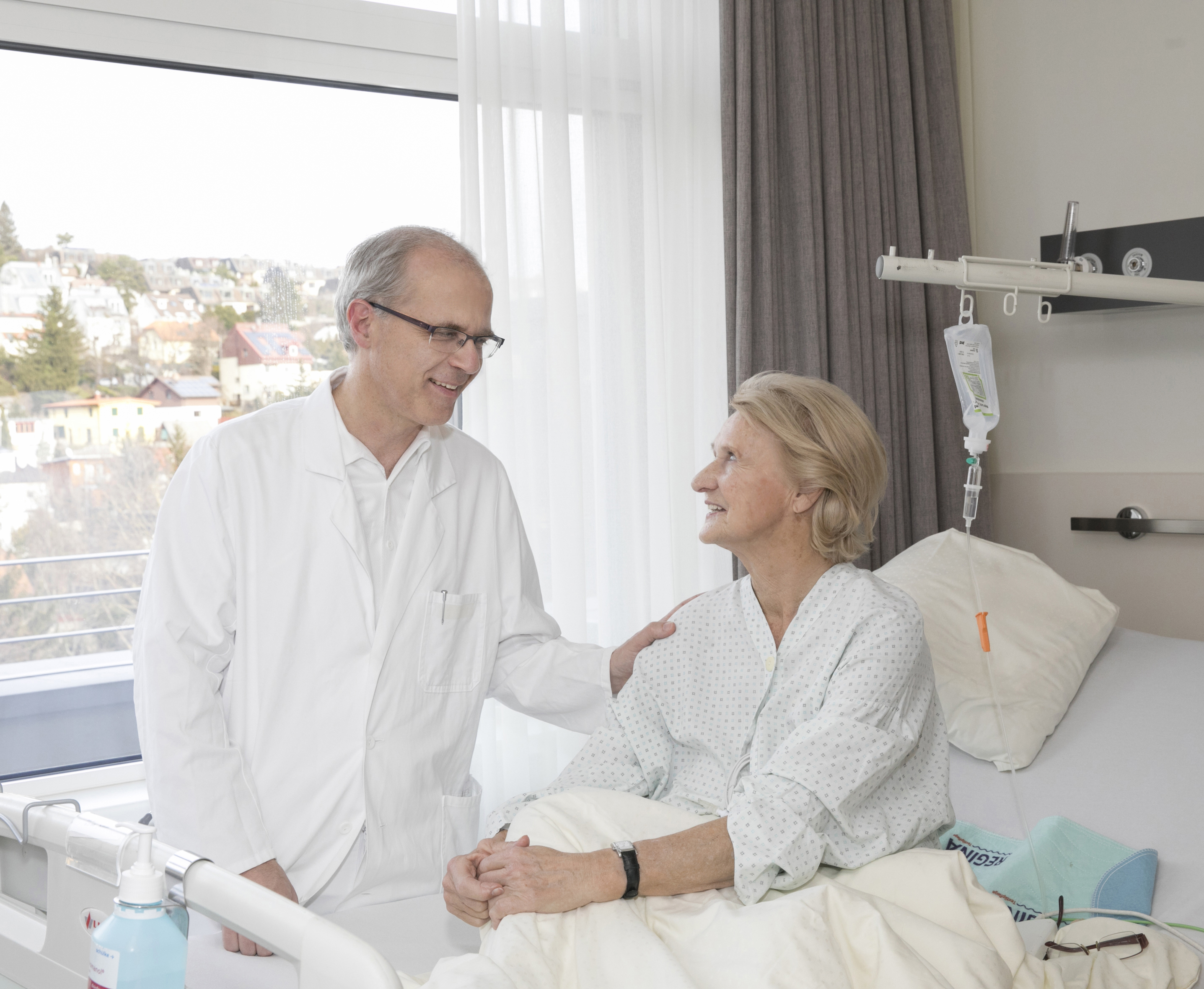Ein Arzt unterhält sich mit einer im Bett sitzenden Patientin