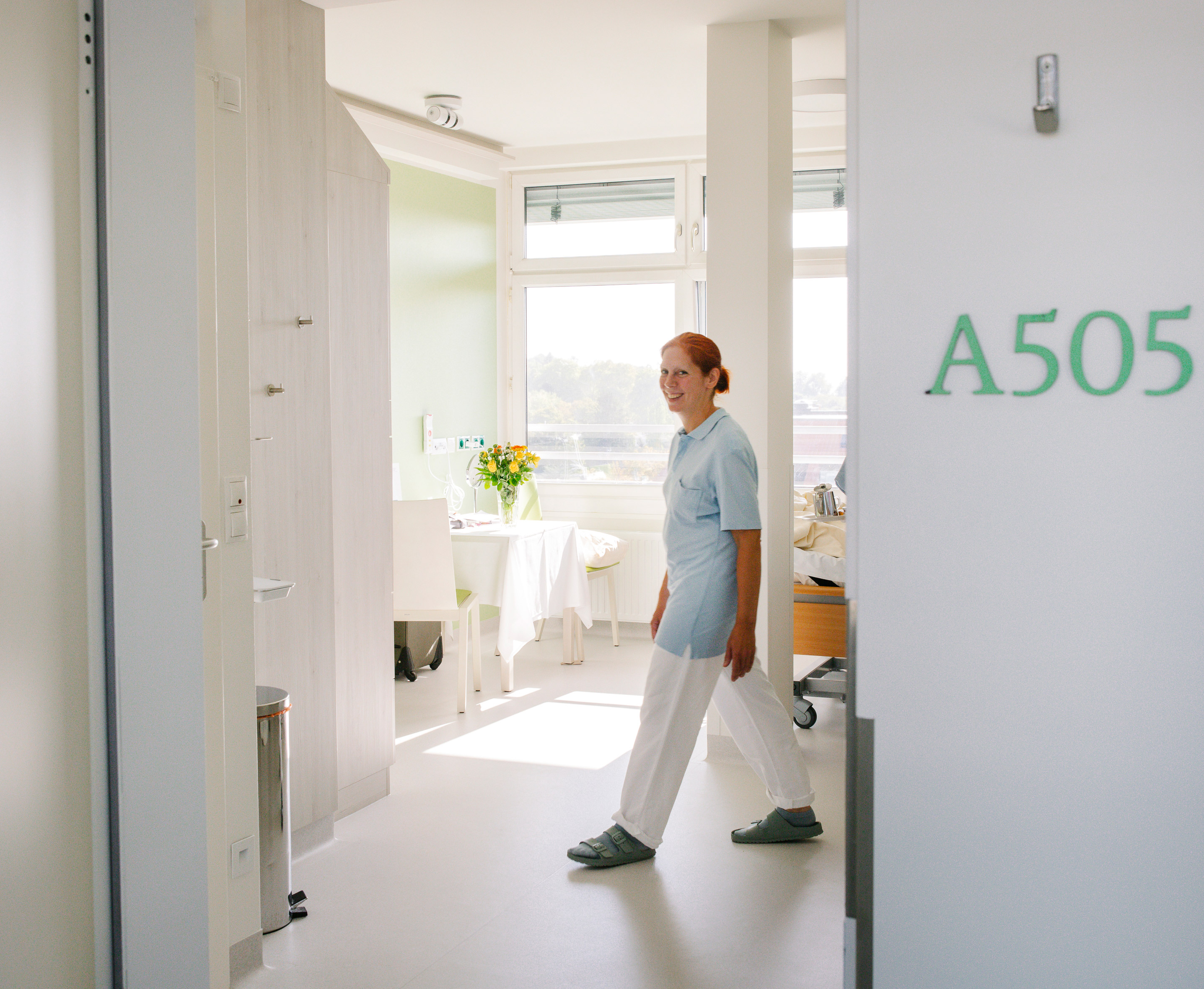 Blick ins Patientenzimmer, eine Ärztin lächelt in die Kamera