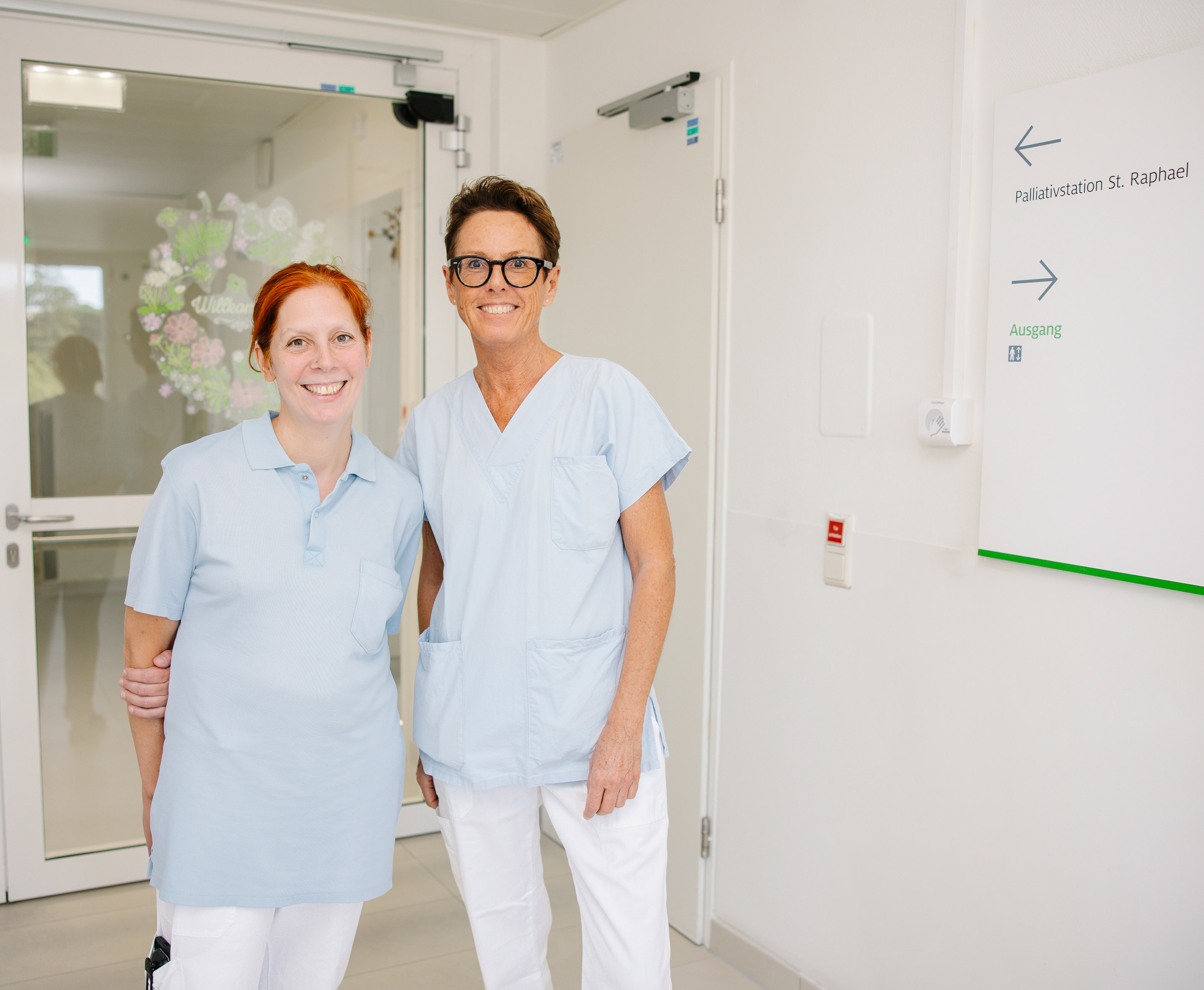 Eine Pflegeperson und eine Ärztin stehen vor dem Eingang zur Palliativstation