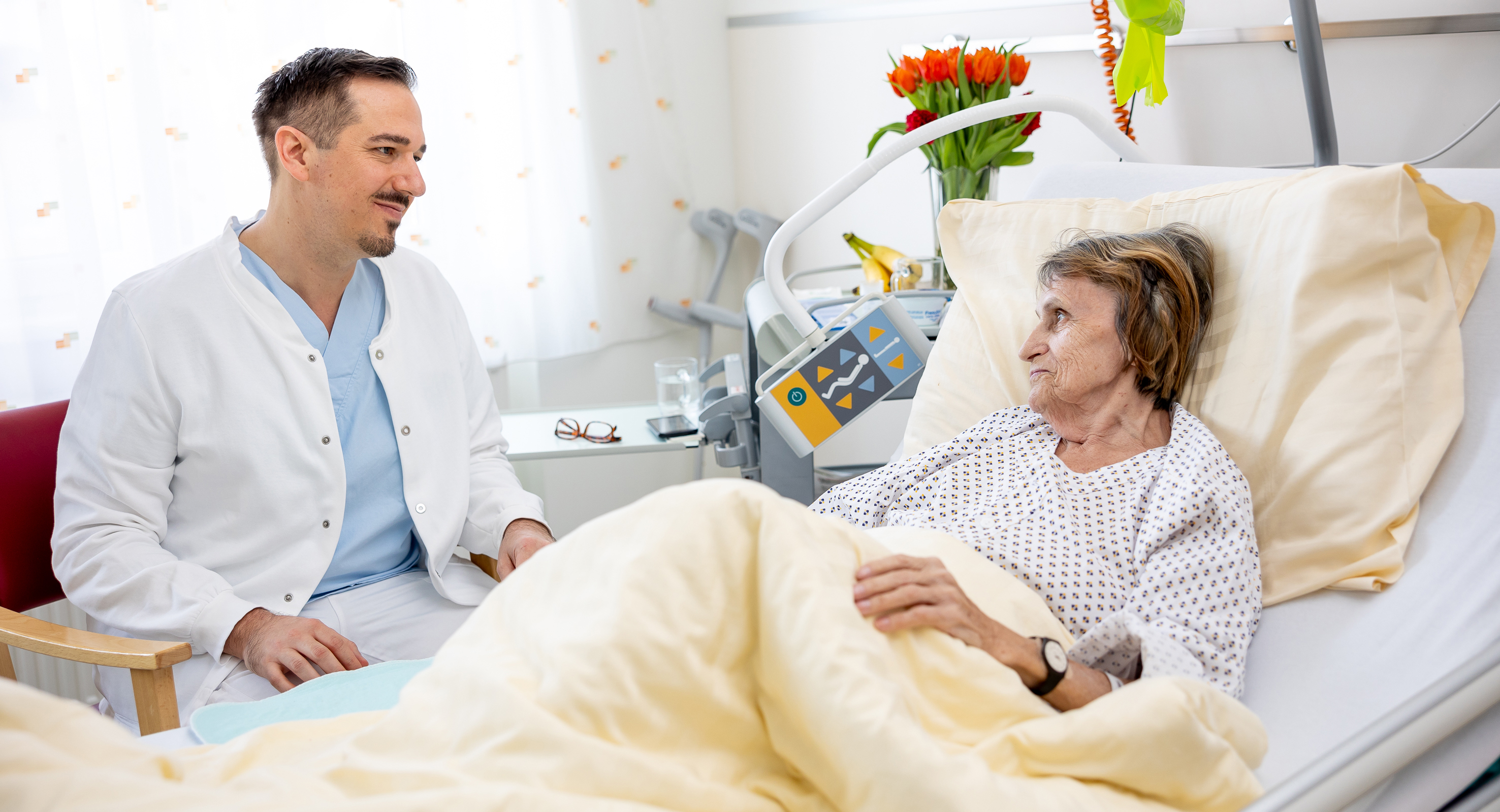 Eine Pflegekraft sitzt am Bett einer Patientin.